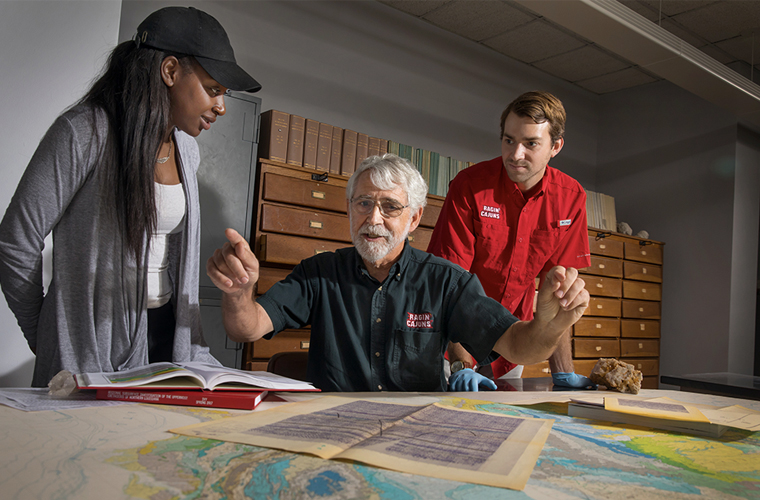 A University of Louisiana at Lafayette research professor looks over maps of the coast line with two students looking over his shoulders