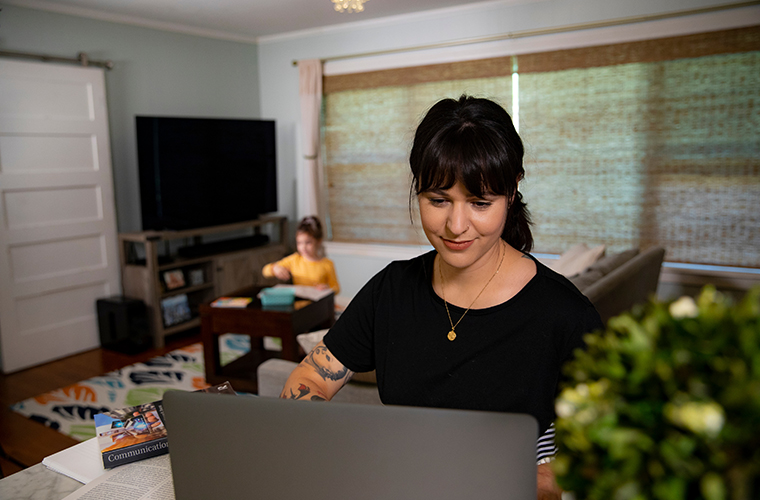 Student at laptop with daughter playing in the background