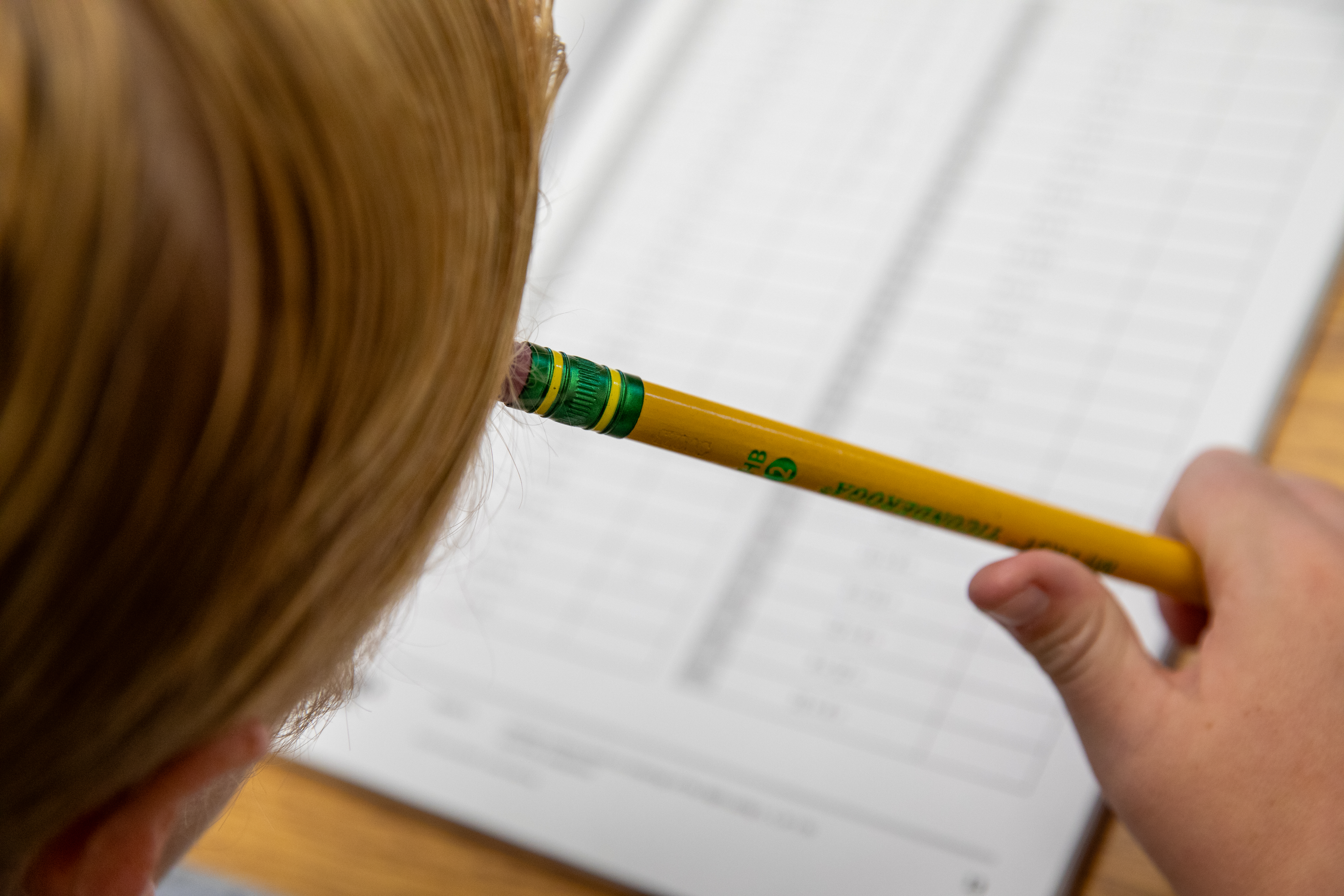 A child sits with their pencil against their forehead as they look over an assessment.