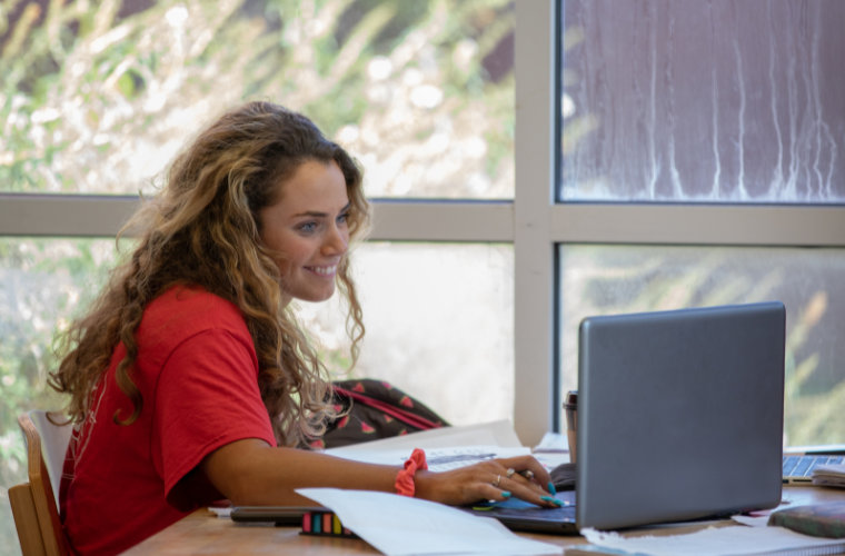 A young girl with a red shirt looking at her computer screen and pushing a key.