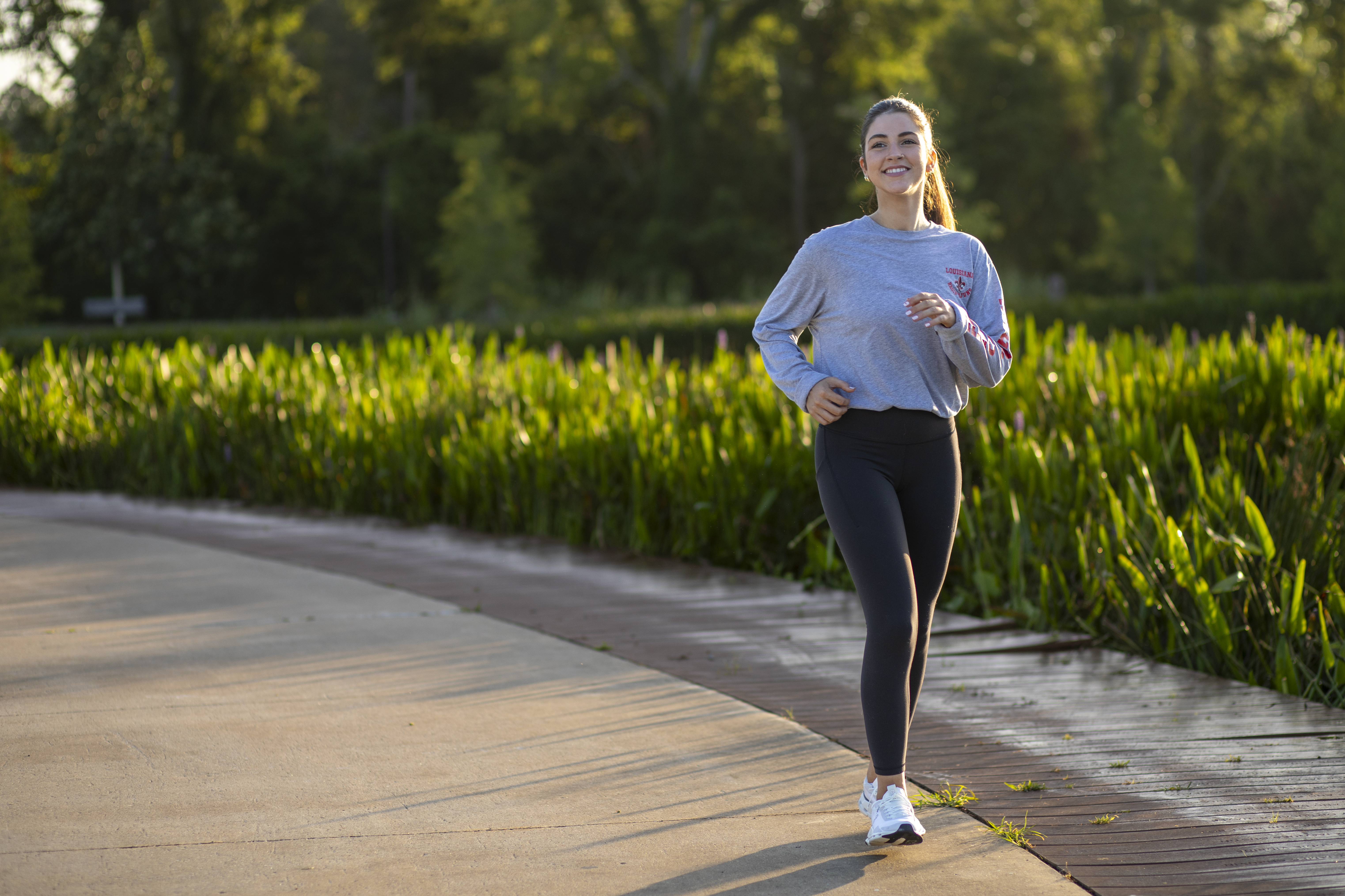 A young woman is pictured running along a cement path lined with greenery.