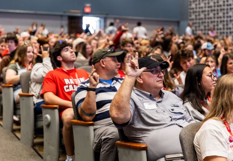 Students attending Orientation sit in a large auditorium, displaying the UL hand sign 
