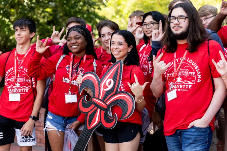 Students attending Orientation pose in matching red t-shirts, holding a fleur de lis sign