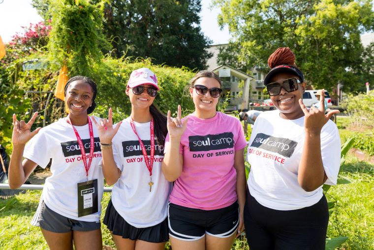 Four students wearing SOUL Camp t-shirts pose in a garden, giving the UL fleur-de-lis hand sign