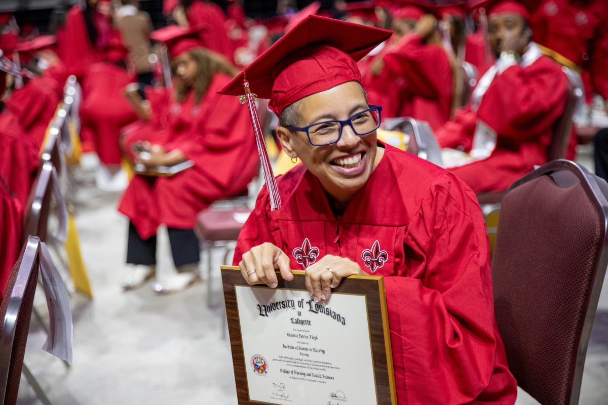 Online RN to BSN graduate smiles in cap and gown holding her newly earned degree.