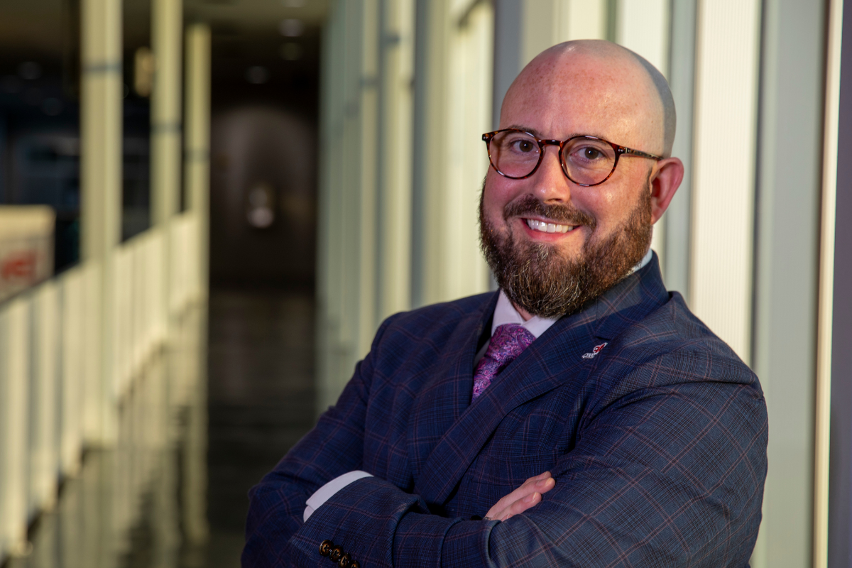 Wearing a suit with a UL Lafayette alumni lapel pin, Brandon Hamilton smiles for a professional portrait in an office setting.