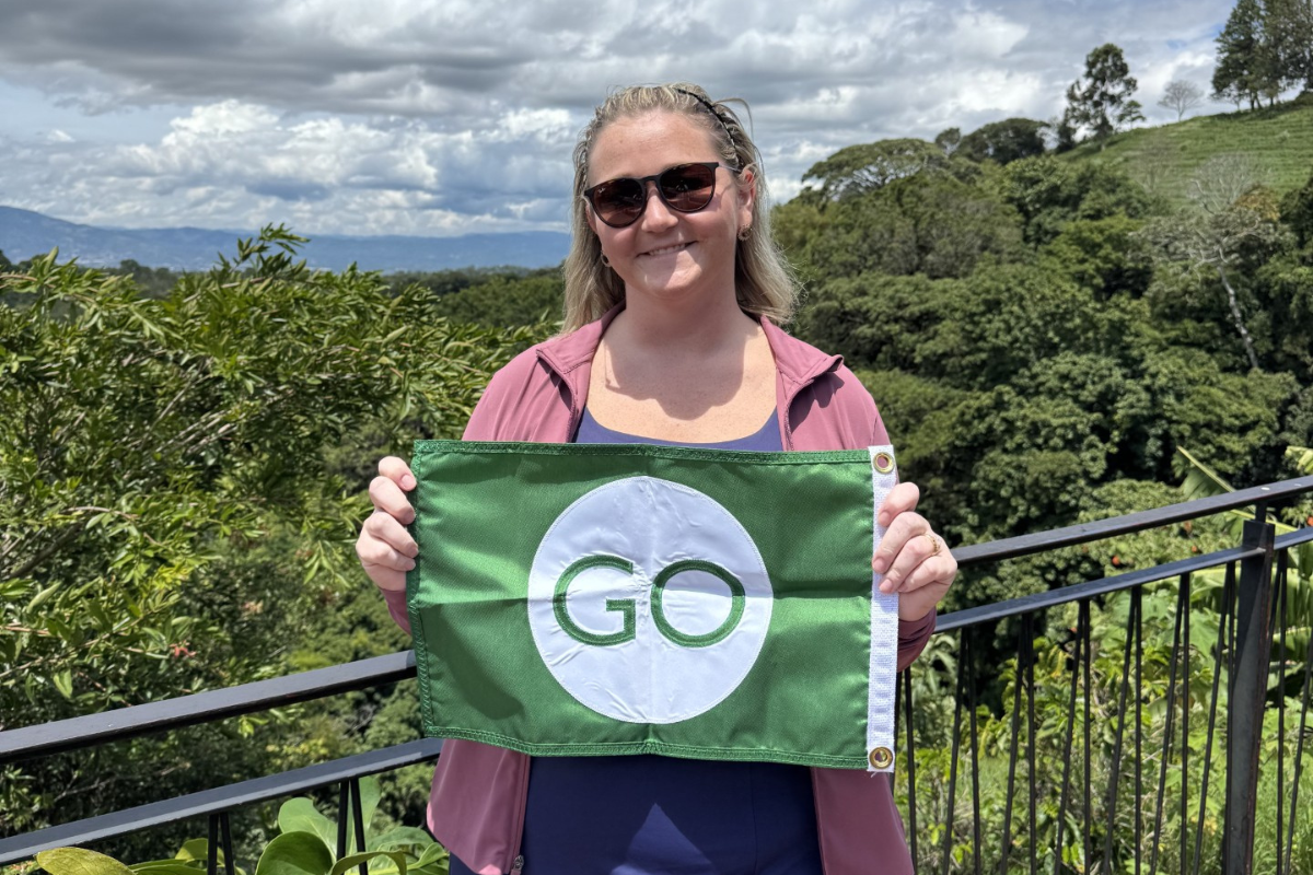 Lauren Schexnider, a first-generation college student and MBA candidate, is pictured in Costa Rica holding a green flag with the word "GO."