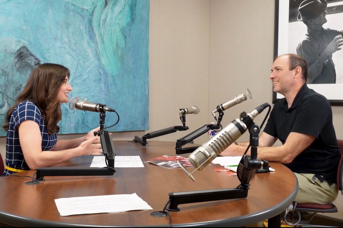 Two people sit across from each other in a recording studio.