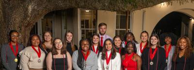 Group of UL Lafayette students wearing cords and medals under an oak tree