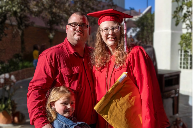 Online health and wellness student smiles with family at UL Lafayette's Commencement..