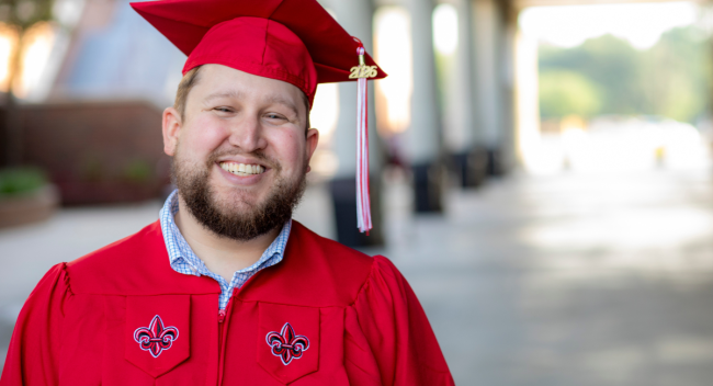 Graduate of the online management bachelor's degree program smiles in his cap and gown after graduating.