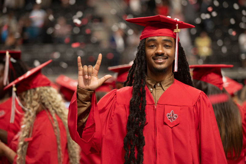 Graduate of the online health services administration degree program smiles in his cap and gown, with confetti falling in the background.