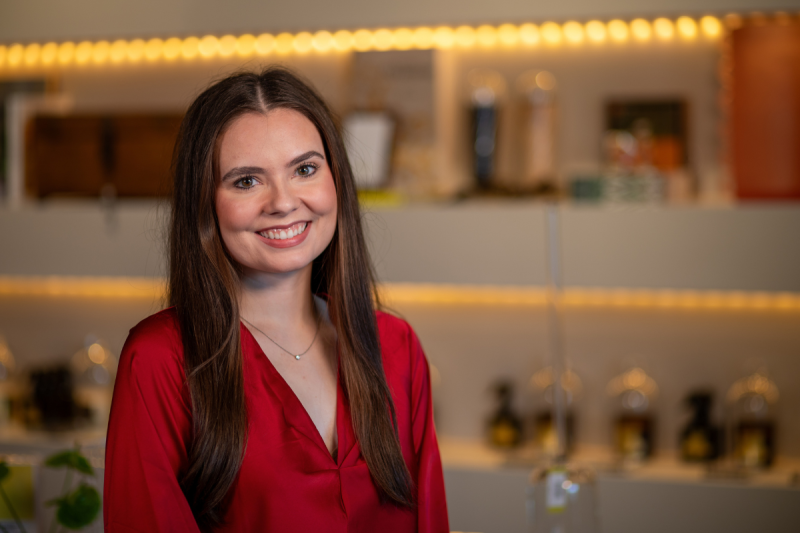 Graduate of UL Lafayette's psychology degree program smiles in front of a store display, wearing a red blouse.